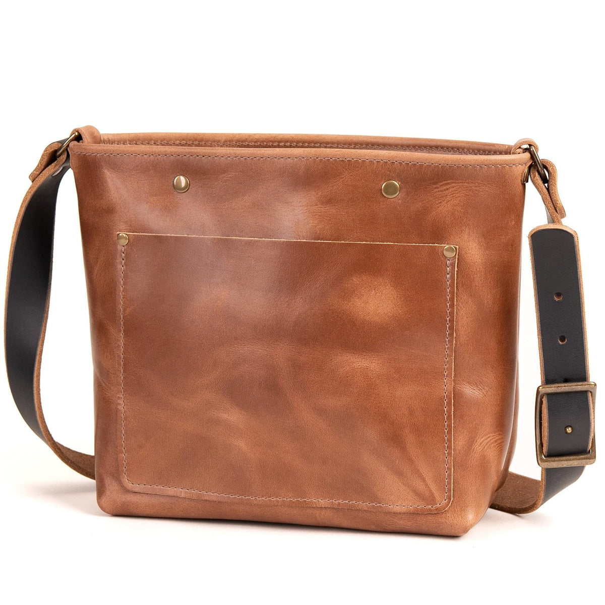 A brown leather crossbody bag with a front pocket, adjustable black strap, and brass-tone hardware, photographed on a clean white background.
