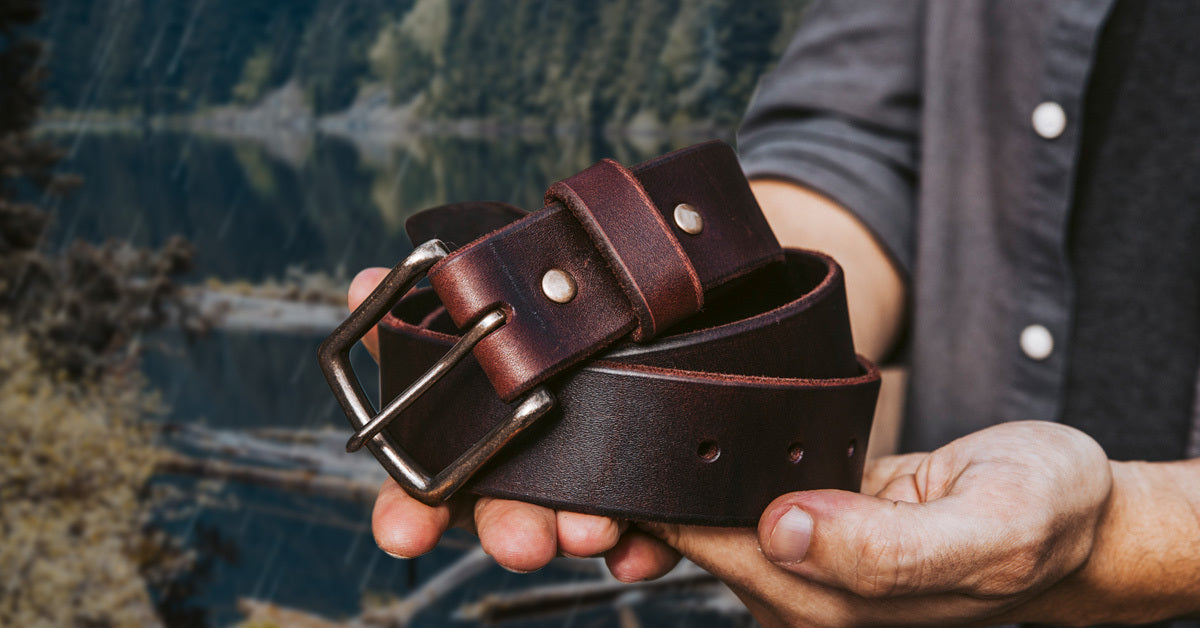 A man holding an Oxblood Leather belt while standing in front of picturesque Canadian scenery.