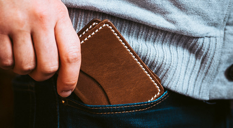 Hand sliding a slim-profile brown leather wallet into a front pocket