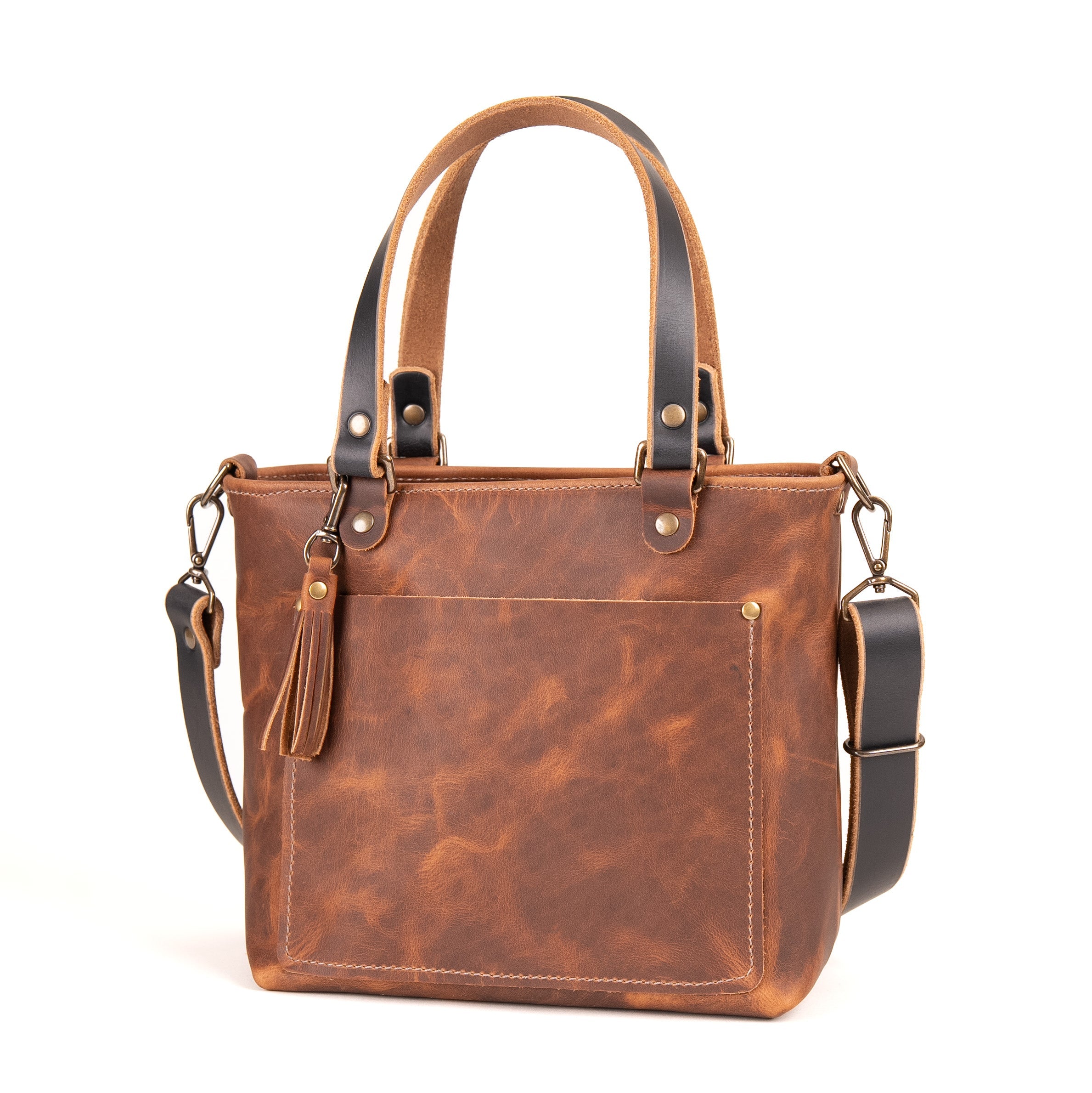 A brown distressed leather tote bag with dark brown leather handles and shoulder strap, featuring brass-tone hardware and a tassel detail, set against a plain white background.