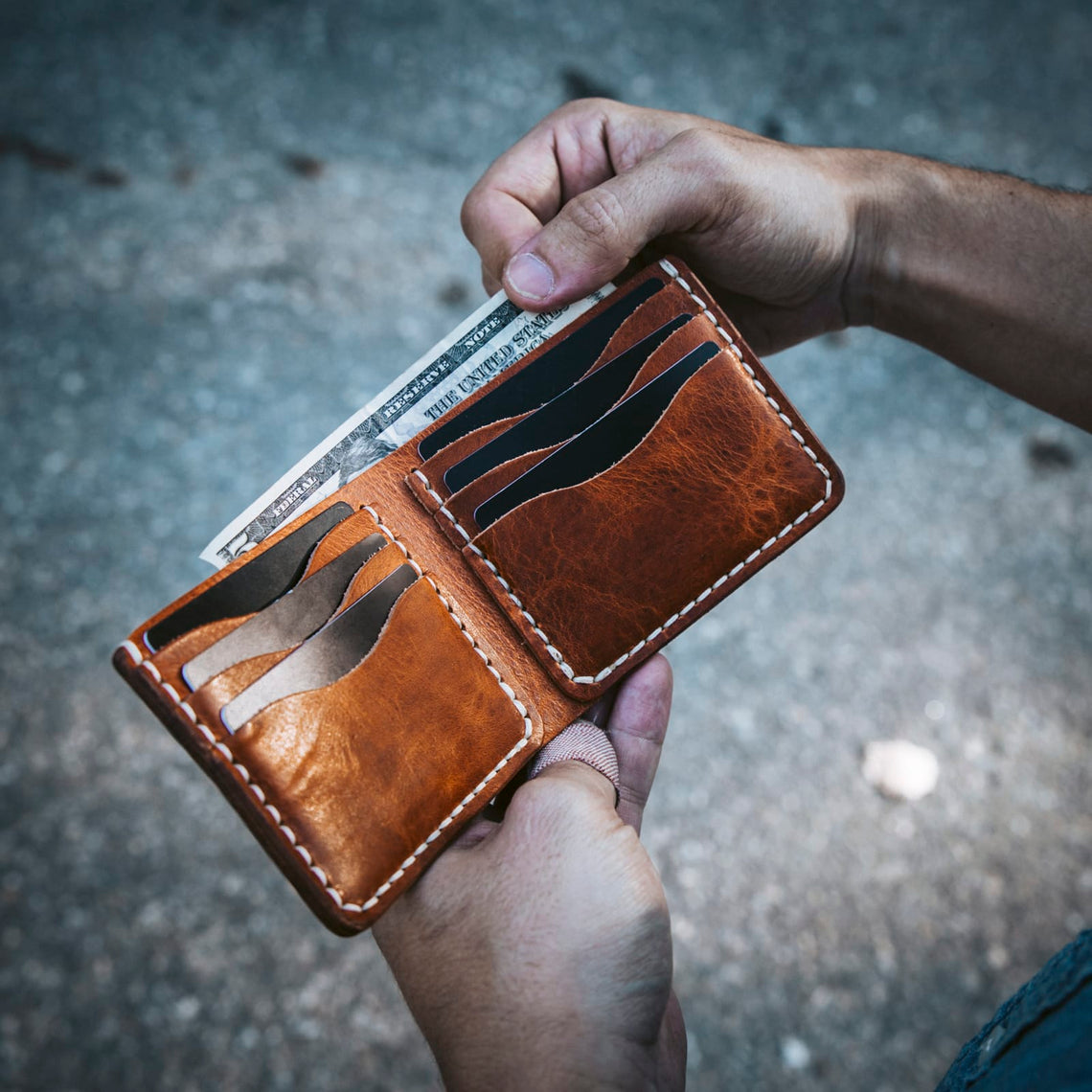 Hand holding a brown leather wallet with credit cards visible.